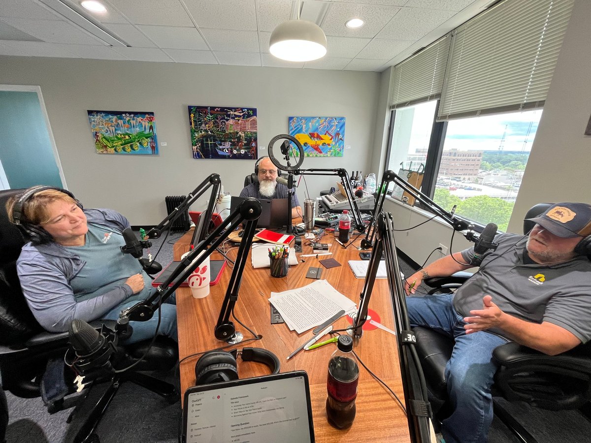 Three people recording a podcast in a studio with microphones, headphones, and equipment on an orange table